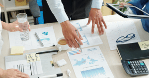 View of table of business papers with two pairs of Caucasian hands in view.